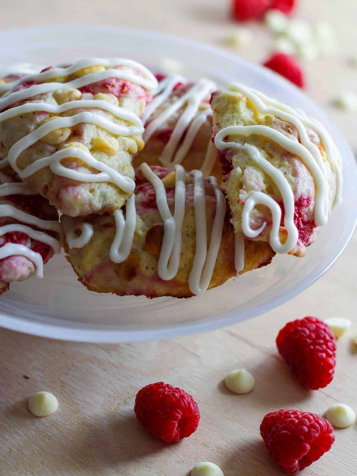 A white small cake plate filled with raspberry scones studded with white chocolate chips and sweet red raspberries.