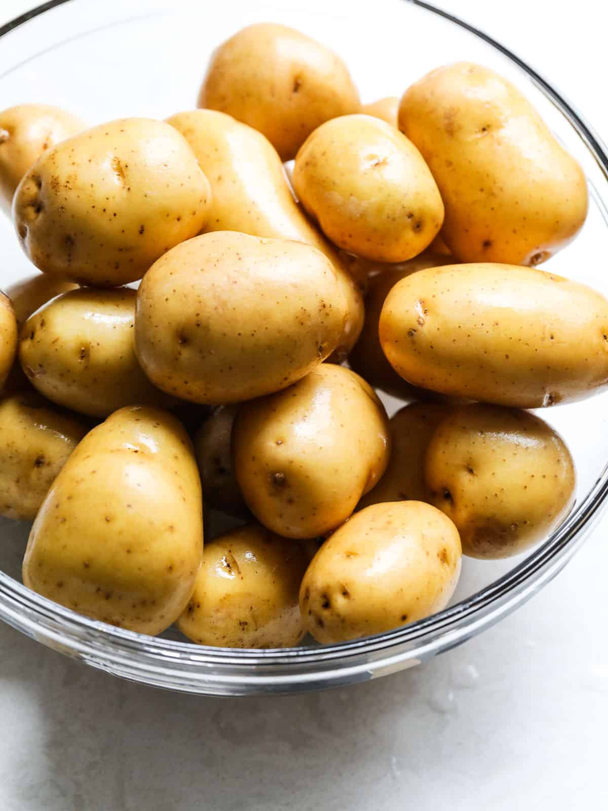 A large clear glass bowl filled with baby potatoes ready to use in a recipe.