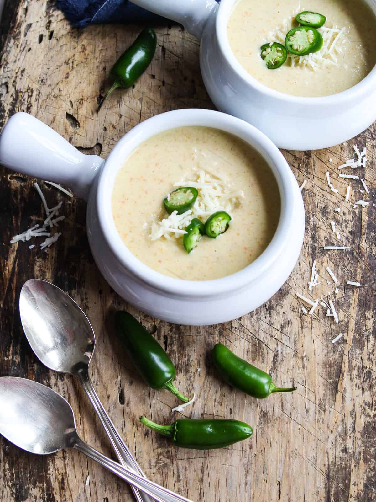 Two silver spoons next to a white handled soup bowl filled with jalapeno popper soup.