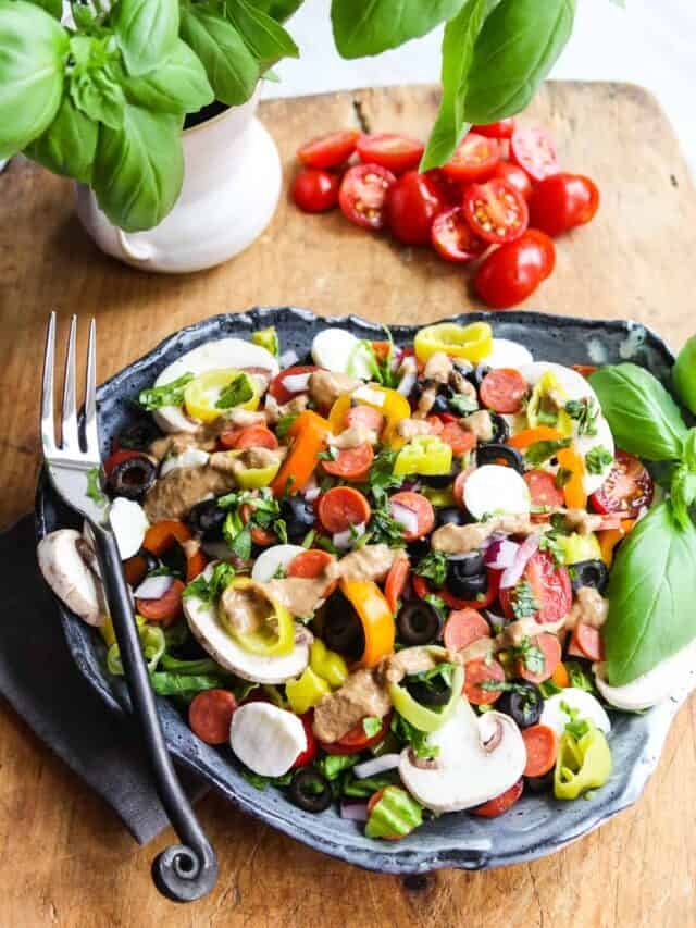 A colorful Pizza Salad loaded with toppings like black olives, mushrooms, mini pepperonis, pepperoncinis, cherry tomatoes, and mini mozzarella balls.