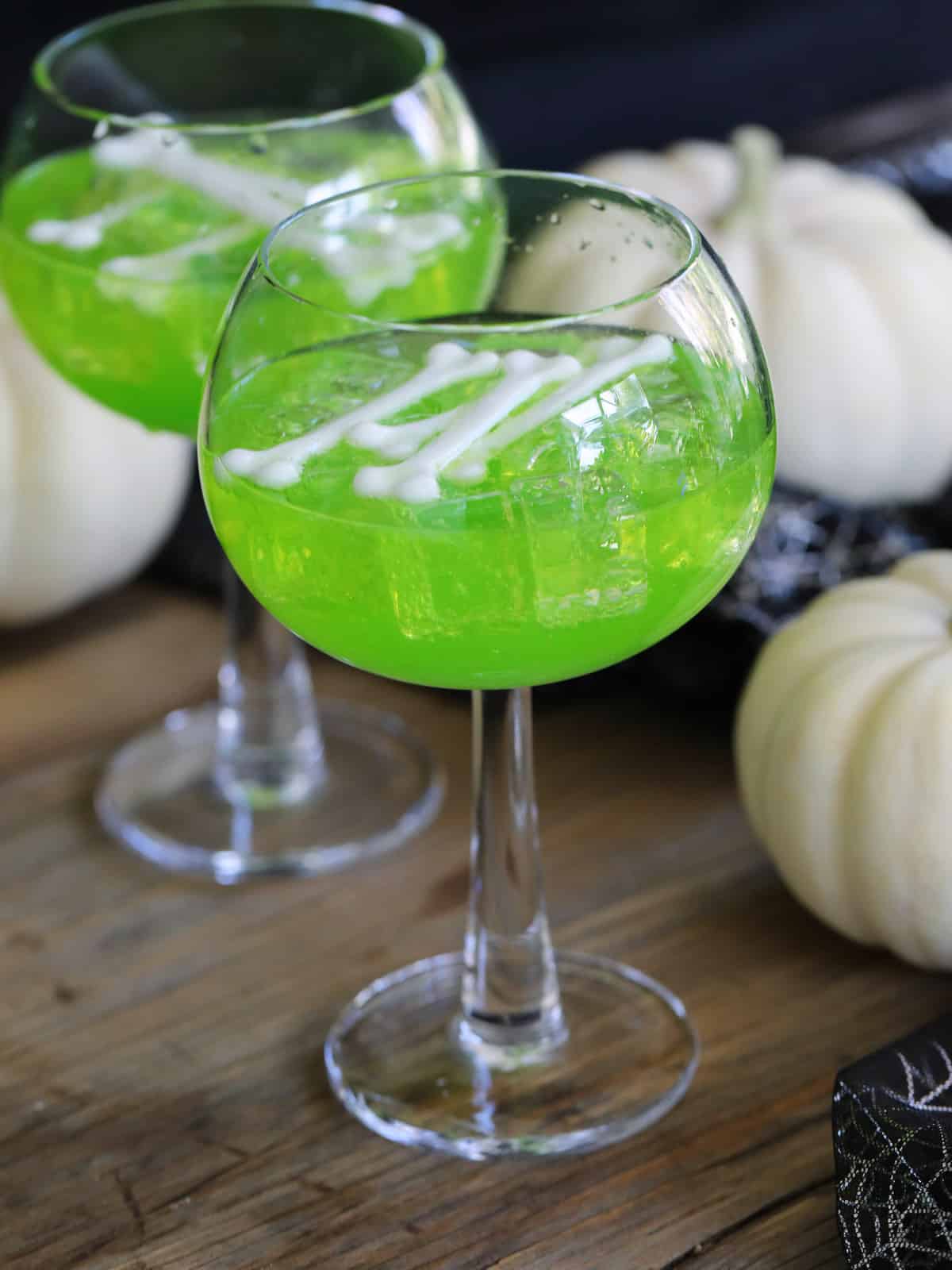 Two tall glasses filled with green drinks for a Halloween party and white bones as a garnish.