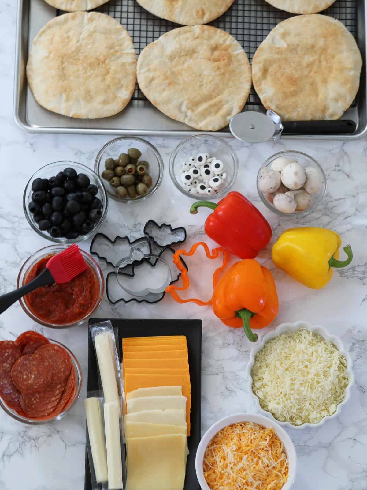 Ingredients to bake Halloween pita pizzas on a baking rack decorated to look like ghosts, pumpkins, dracula, frankenstein, and monsters.