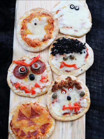 Six baked Halloween pizzas on a baking rack decorated to look like ghosts, pumpkins, dracula, frankenstein, and monsters.