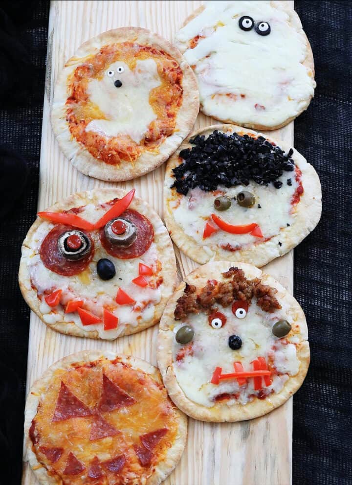 Six baked Halloween pizzas on a baking rack decorated to look like ghosts, pumpkins, dracula, frankenstein, and monsters.
