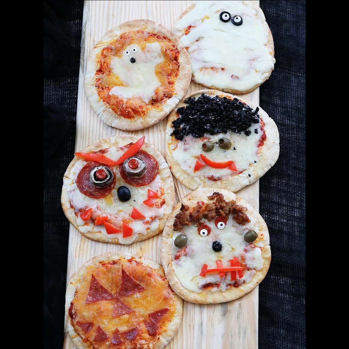 Six baked Halloween pizzas on a baking rack decorated to look like ghosts, pumpkins, dracula, frankenstein, and monsters.