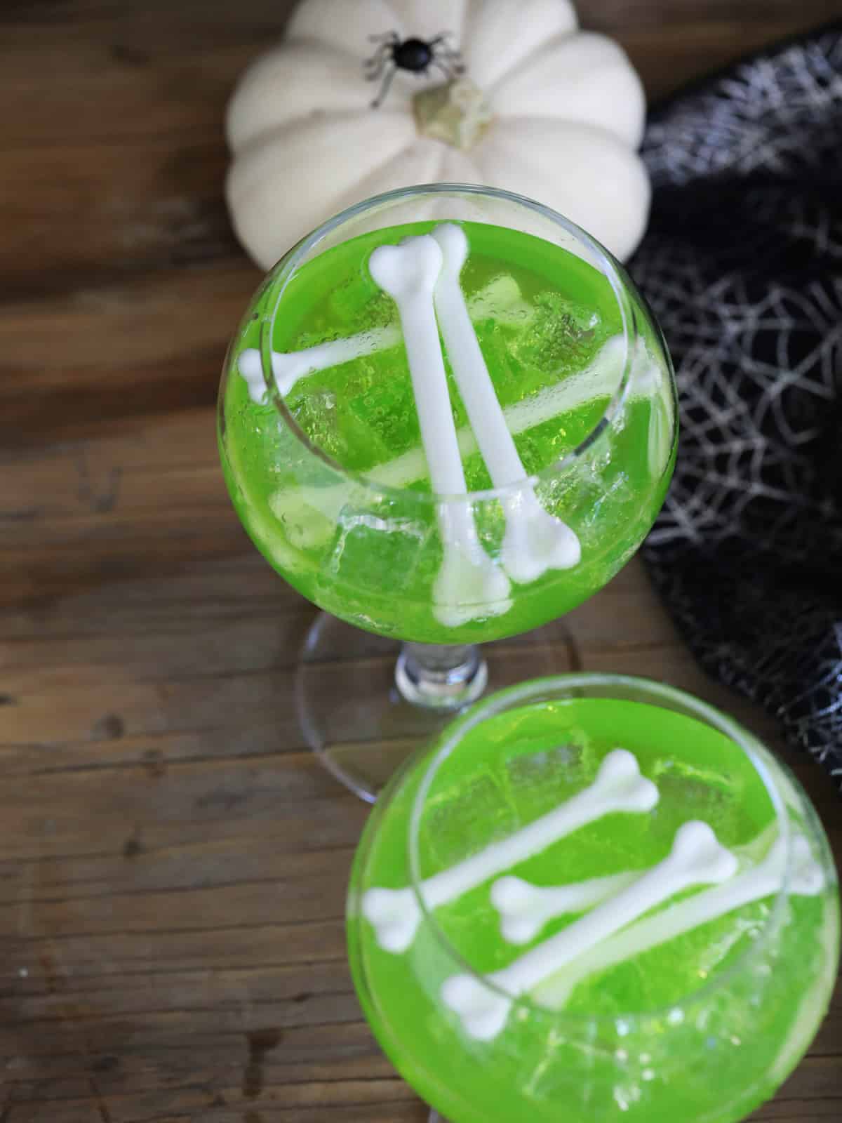 Looking down on two glasses with green Midori vodka drinks garnished with white bones.