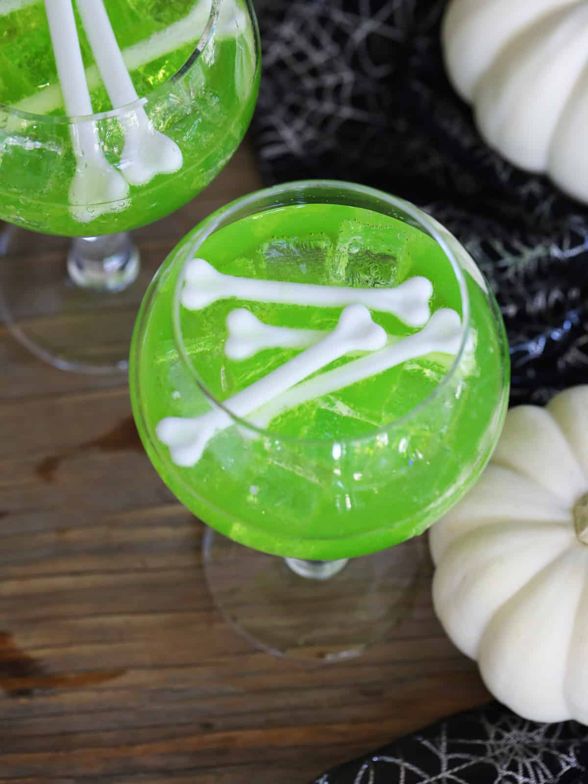 Looking down on Halloween party with two Witches brew midori sours garnished with white plastic bones for Halloween cocktails.