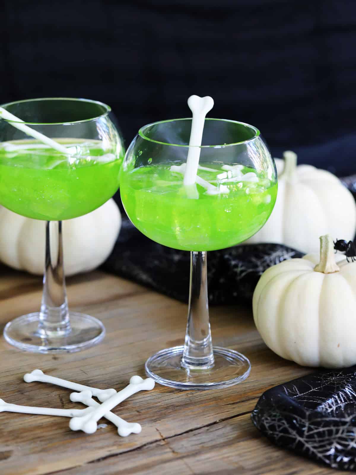 A Halloween party with two green MIdori sour vodka cocktails and garnished with white plastic bones for Halloween cocktails.