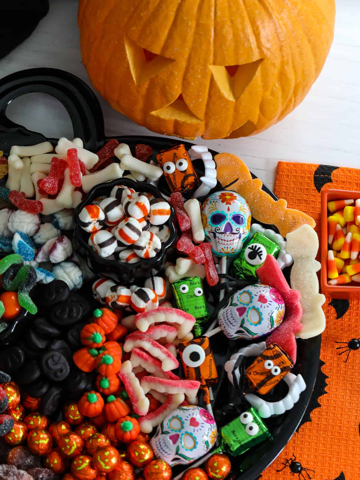 A Halloween candy board on a black tray loaded with cute candy for a party including pumpkins, licorice, mints, lollipops and gummy candy.