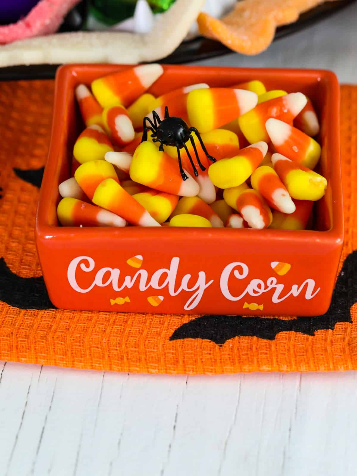 Close up of an orange square dish filled with candy corn that says candy corn on the front.