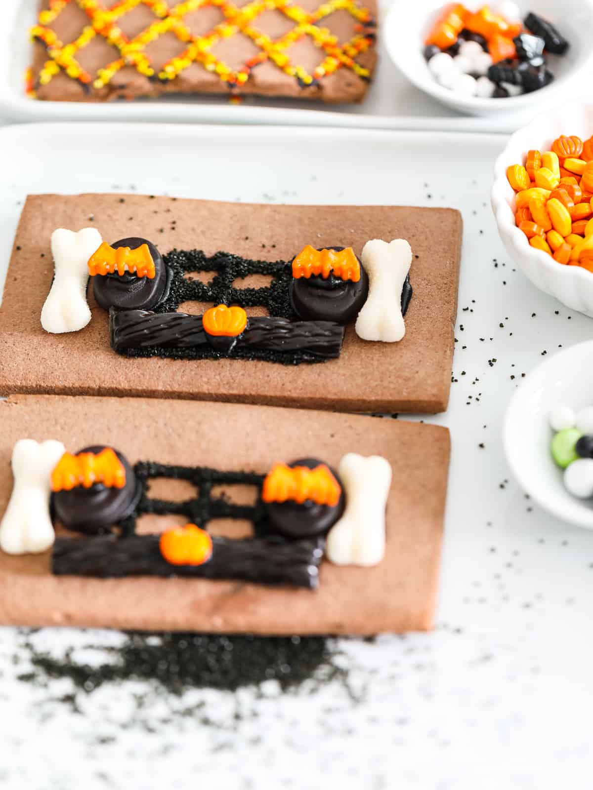 Two pieces of a Halloween gingerbread house decorated with candy laying on a white plate.
