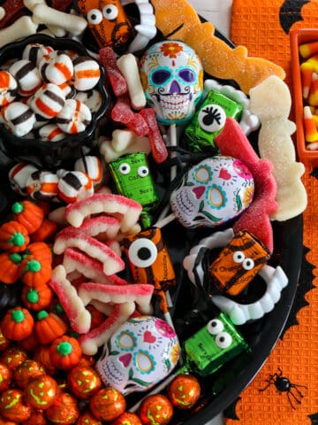 A Halloween candy board on a black tray loaded with cute candy for a party including pumpkins, licorice, mints, lollipops and gummy candy.