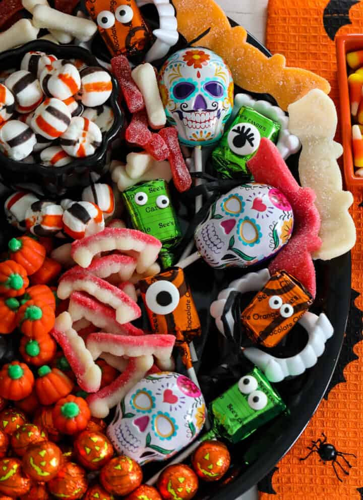 A Halloween candy board on a black tray loaded with cute candy for a party including pumpkins, licorice, mints, lollipops and gummy candy.