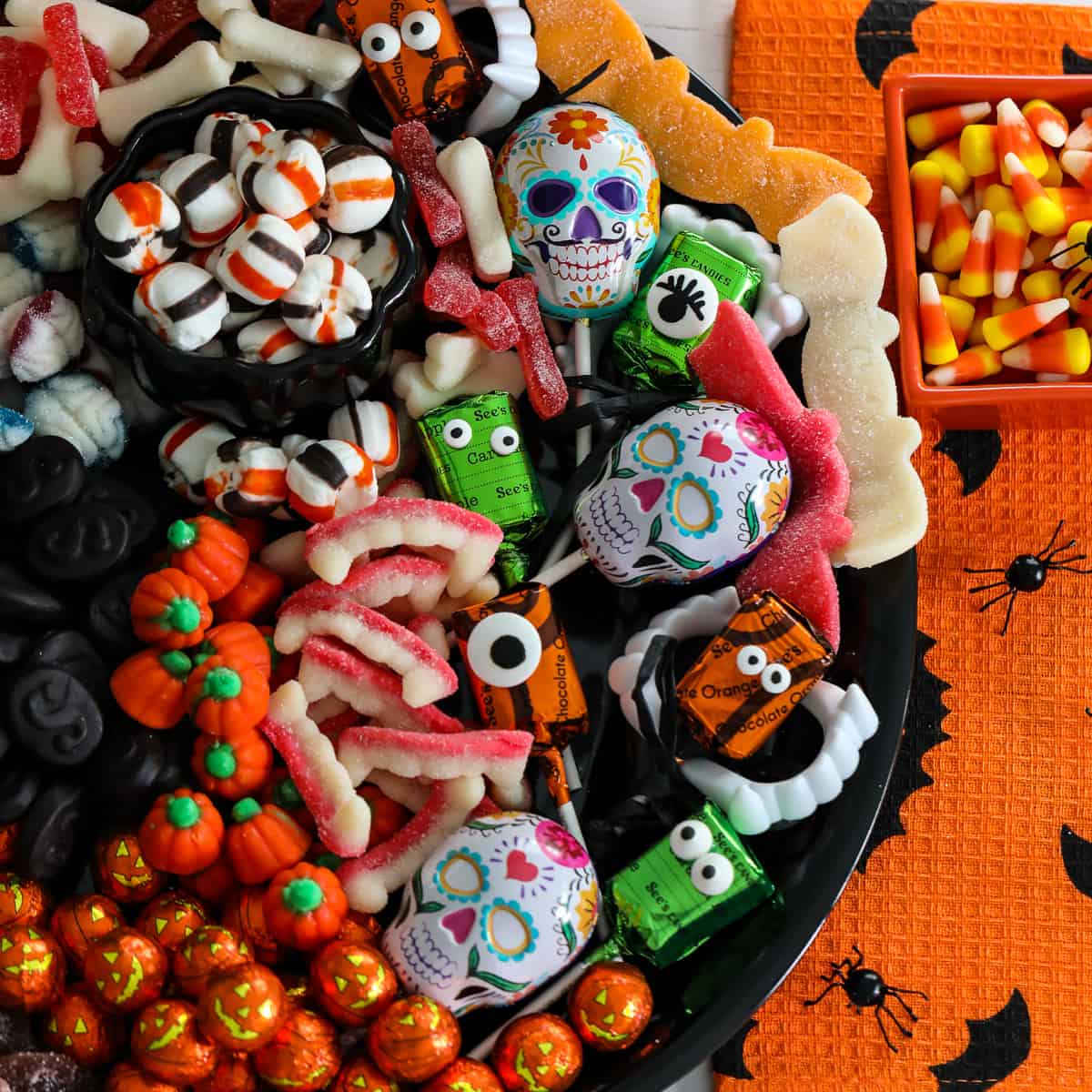 A Halloween candy board on a black tray loaded with cute candy for a party including pumpkins, licorice, mints, lollipops and gummy candy.