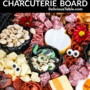 A large Halloween Charcuterie cheeseboard loaded with stacks of crackers, cut and sliced meats, nuts, and Halloween candy for a Halloween party.