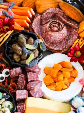 A large Halloween Charcuterie cheeseboard loaded with stacks of crackers, cut and sliced meats, nuts, and Halloween candy for a Halloween party.