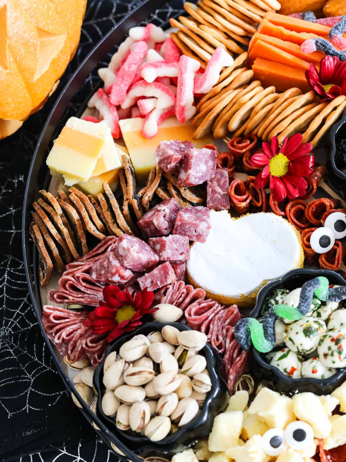 Looking down on a Halloween charcuterie board with pumpkin shaped brie cheese, stacks of crackers, sliced cheeses, nuts, and spooky Halloween candy.