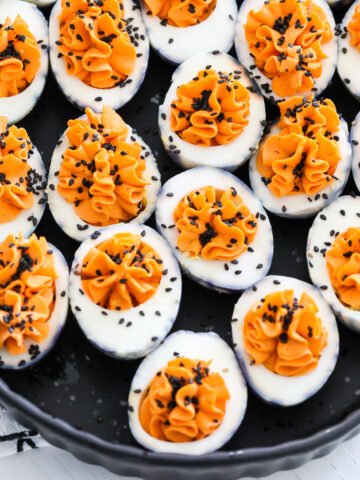 A black platter filled with Halloween deviled eggs sprinkled with black sesame seeds.