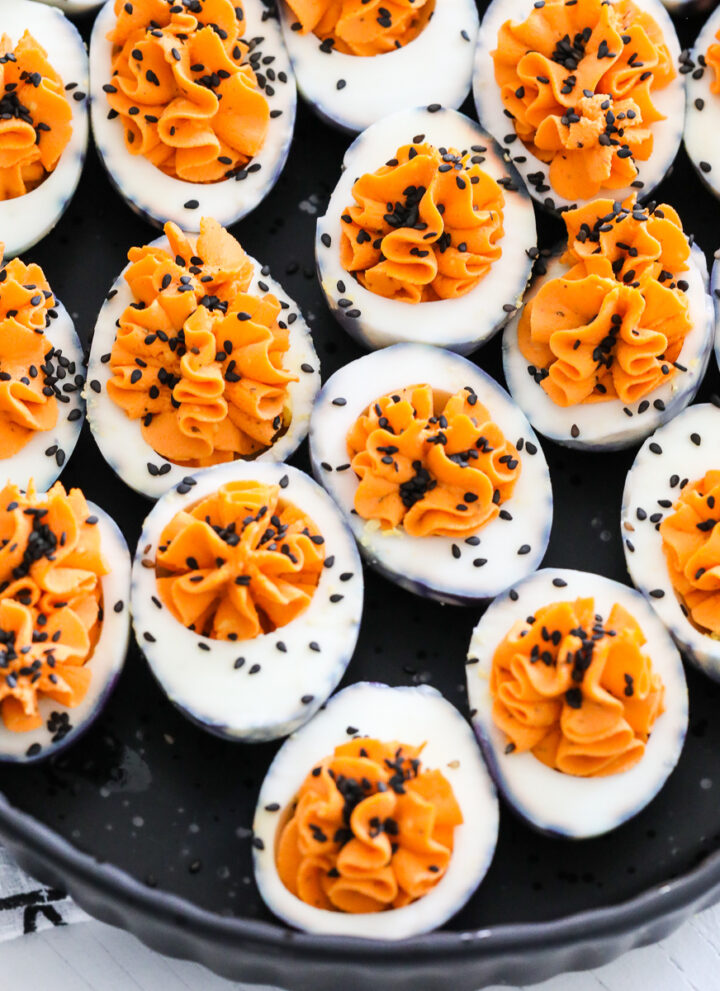 A black platter filled with Halloween deviled eggs sprinkled with black sesame seeds.