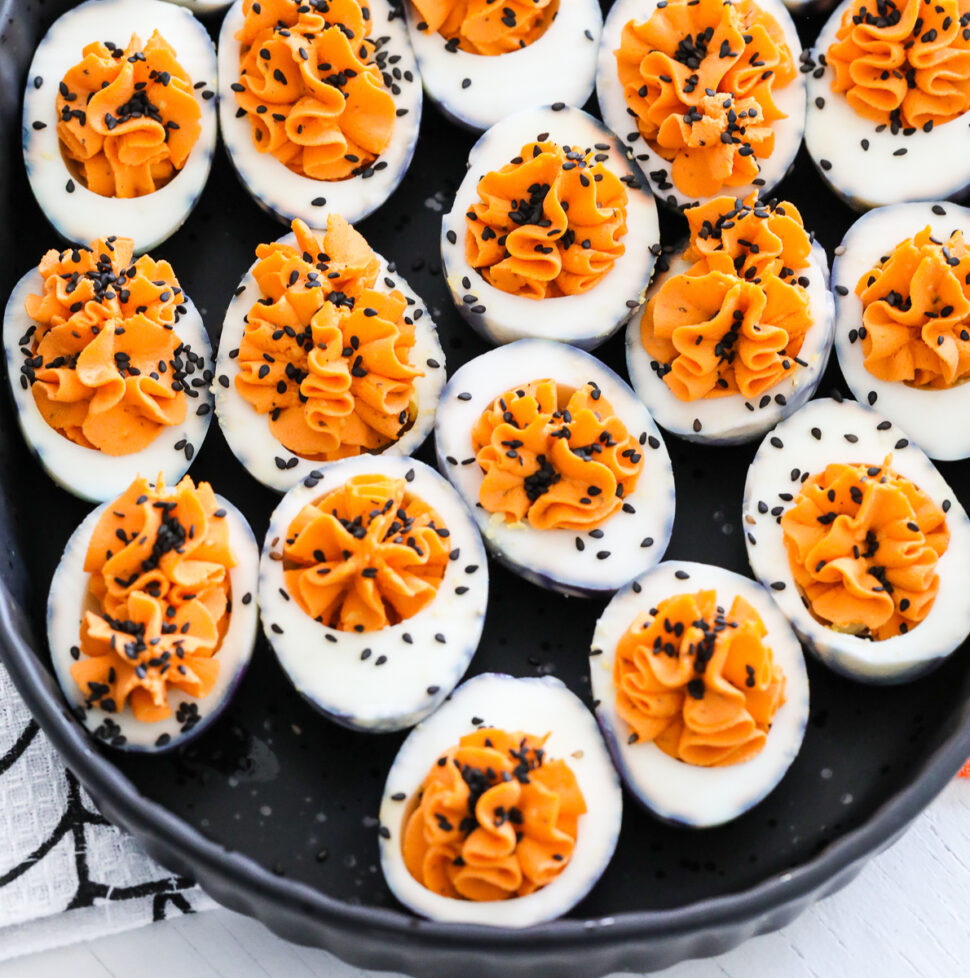 A black platter filled with Halloween deviled eggs sprinkled with black sesame seeds.