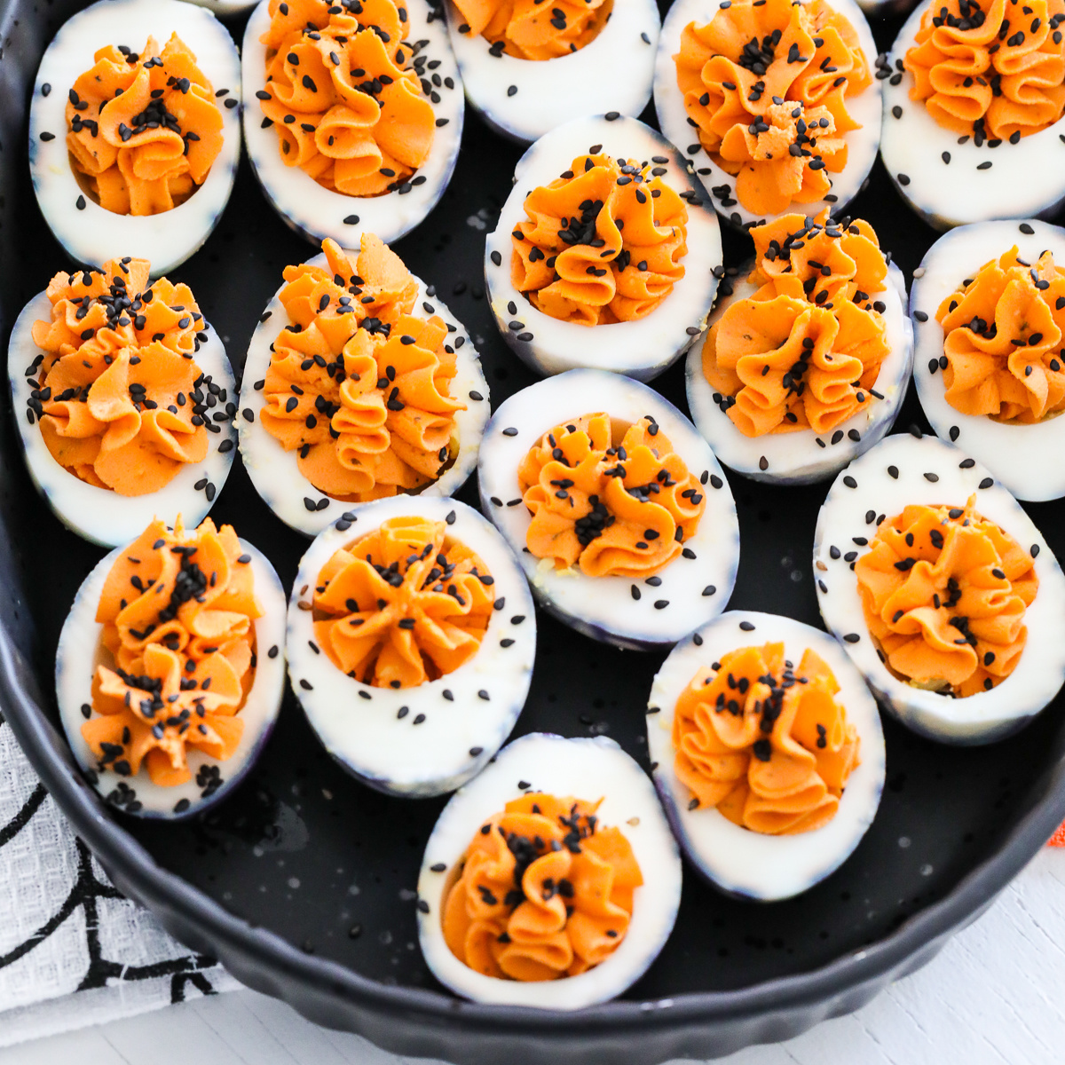 A black platter filled with Halloween deviled eggs sprinkled with black sesame seeds.