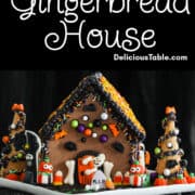 A Halloween gingerbread house decorated with royal icing and candy in orange, black, and white candy with a ghost opening the front door.