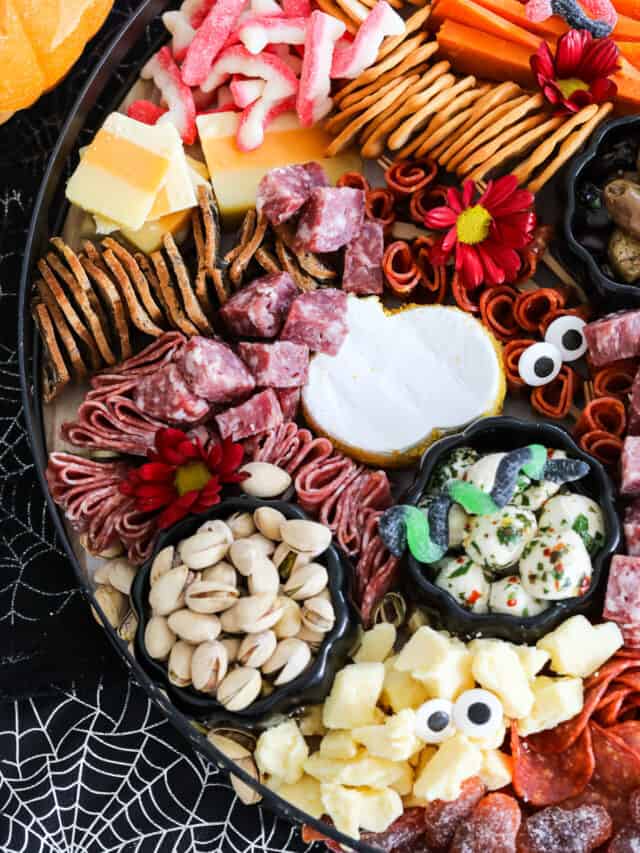 A Halloween charcuterie board filled with cheeses, meat, nuts, candy and more with candy eyeballs and gummy worms.