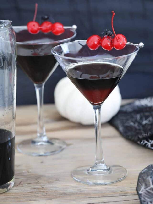 Two martini glasses filled with black vodka and garnished with 3 red cherries at a Halloween party.