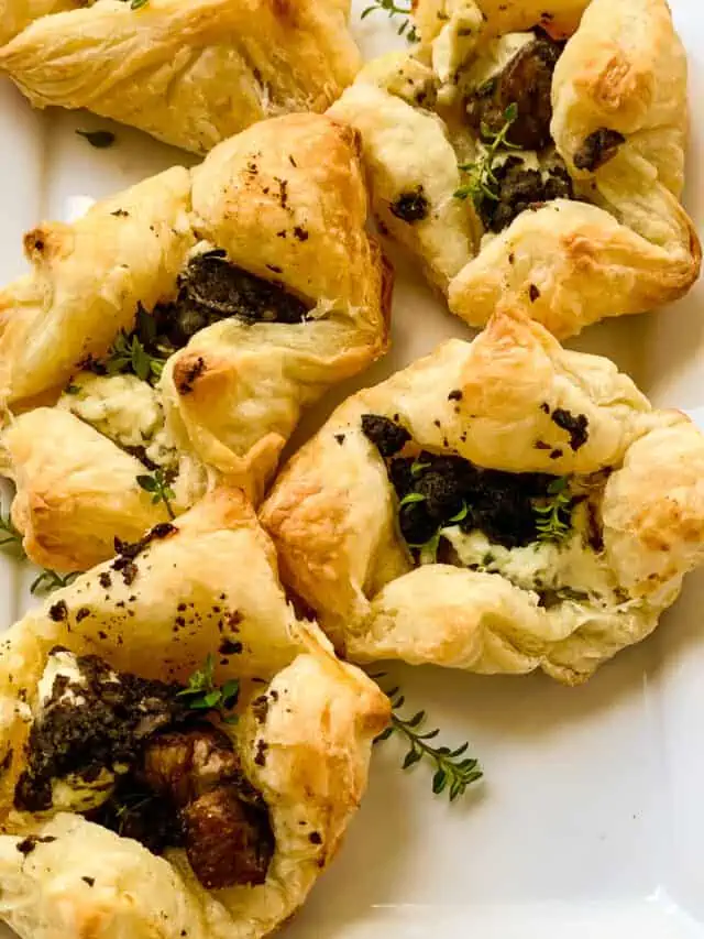 Five freshly baked puff pastry beef wellington appetizers on a rectangle white platter.