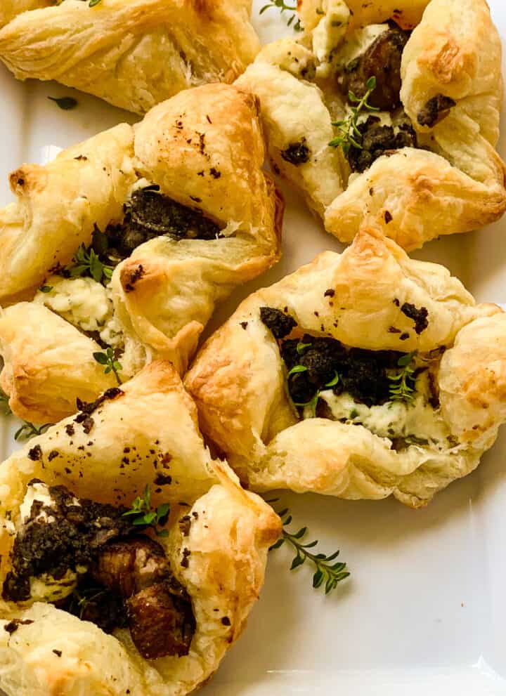 Five freshly baked puff pastry beef wellington appetizers on a rectangle white platter.