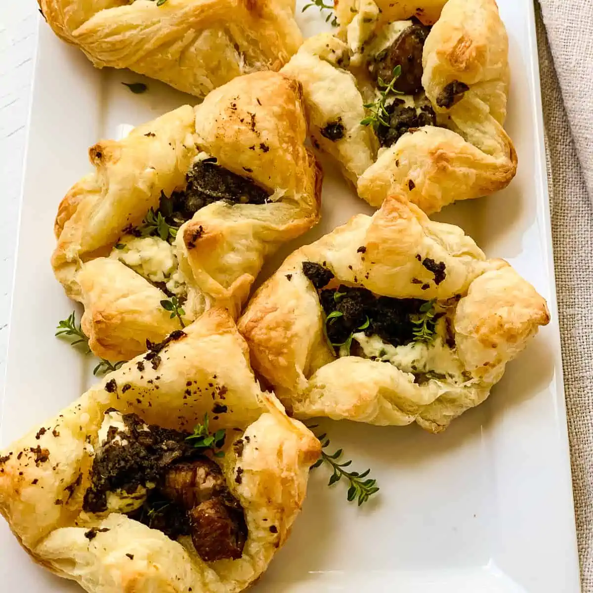 Five freshly baked puff pastry beef wellington appetizers on a rectangle white platter.
