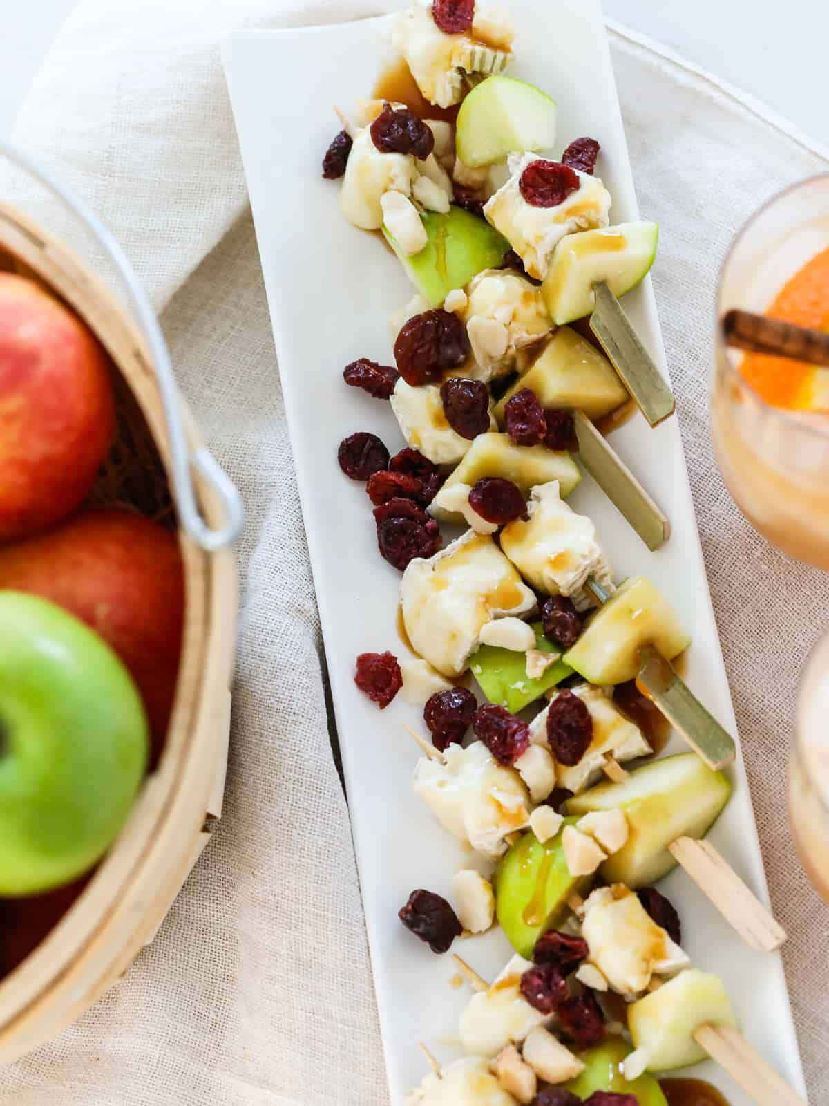 Close up of green apple brie skewers drizzled with caramel sauce on a platter with drinks nearby.