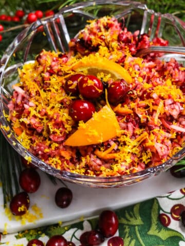 A gorgeous red and orange cranberry relish in a clear crystal bowl with a spoon.