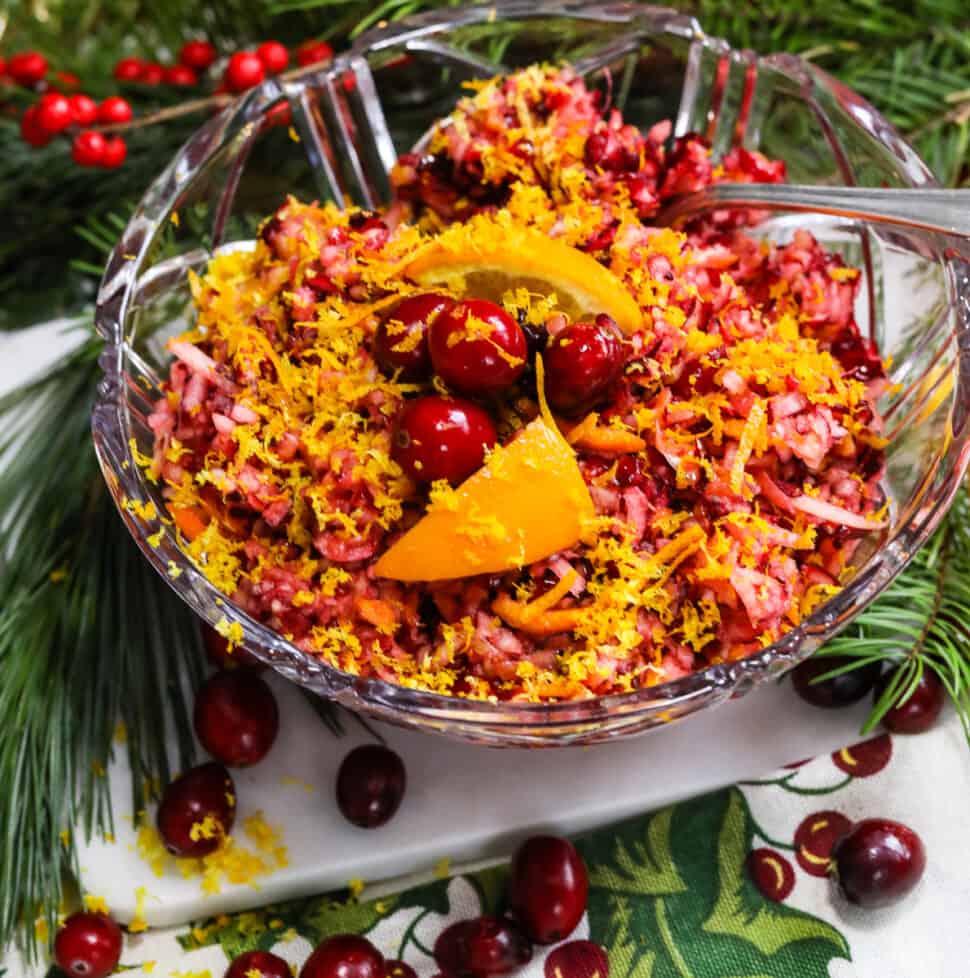 A gorgeous red and orange cranberry relish in a clear crystal bowl with a spoon.