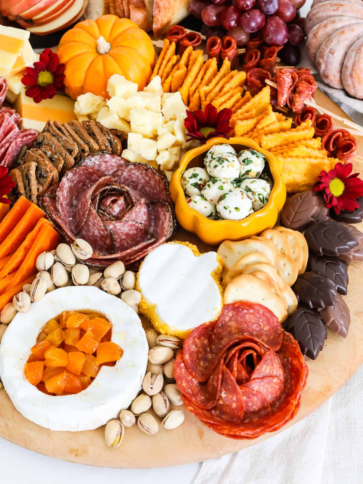 A round cheeseboard filled with assorted cut cheeses and charcuterie meats for a Thanksgiving day feast. 