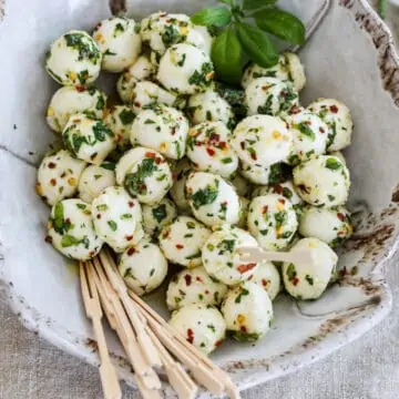 Marinated mozzarella balls in a beige ceramic dish with appetizer toothpicks.