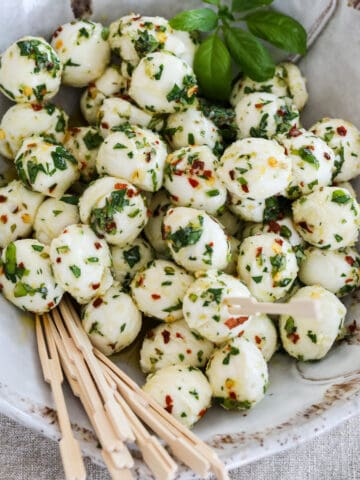 Marinated mozzarella balls in a beige ceramic dish with appetizer toothpicks.