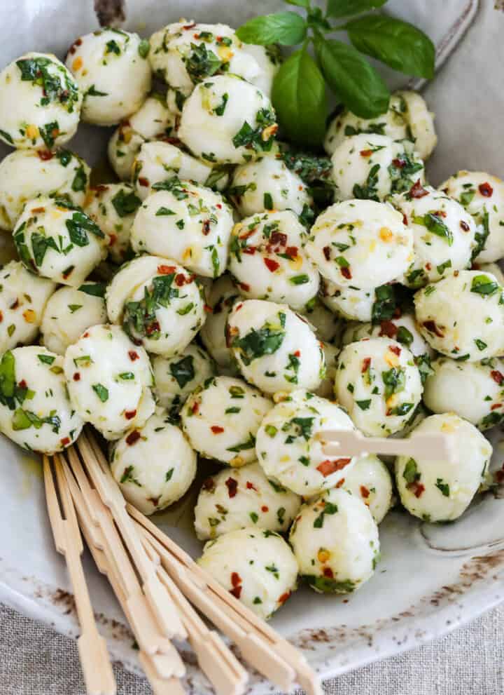 Marinated mozzarella balls in a beige ceramic dish with appetizer toothpicks.