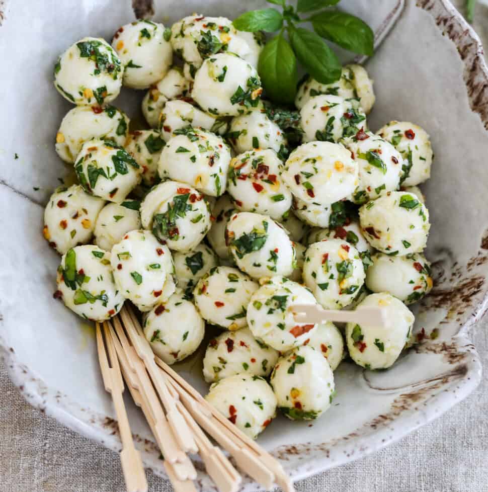 Marinated mozzarella balls in a beige ceramic dish with appetizer toothpicks.