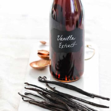 A glass flip top bottle filled with vanilla extract, and real vanilla bean pods on the table.