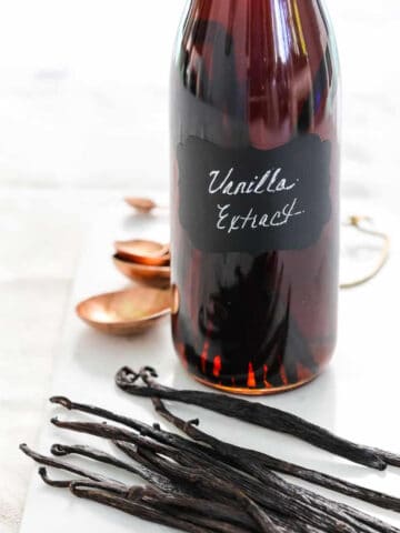 A glass flip top bottle filled with vanilla extract, and real vanilla bean pods on the table.