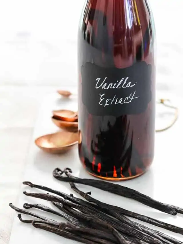 A glass flip top bottle filled with vanilla extract, and real vanilla bean pods on the table.