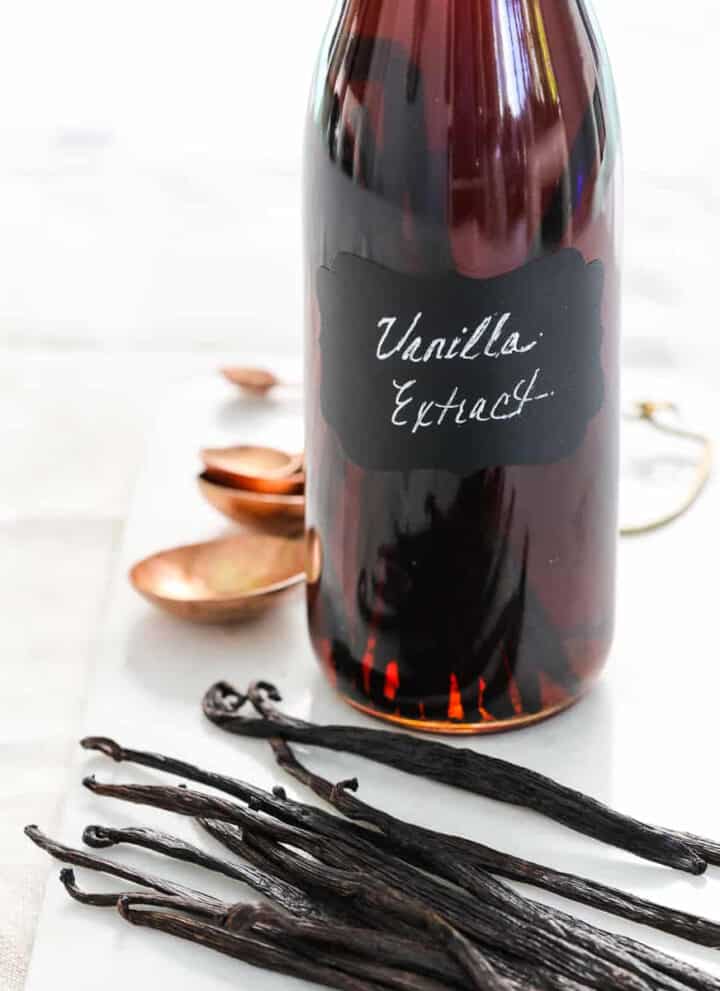 A glass flip top bottle filled with vanilla extract, and real vanilla bean pods on the table.