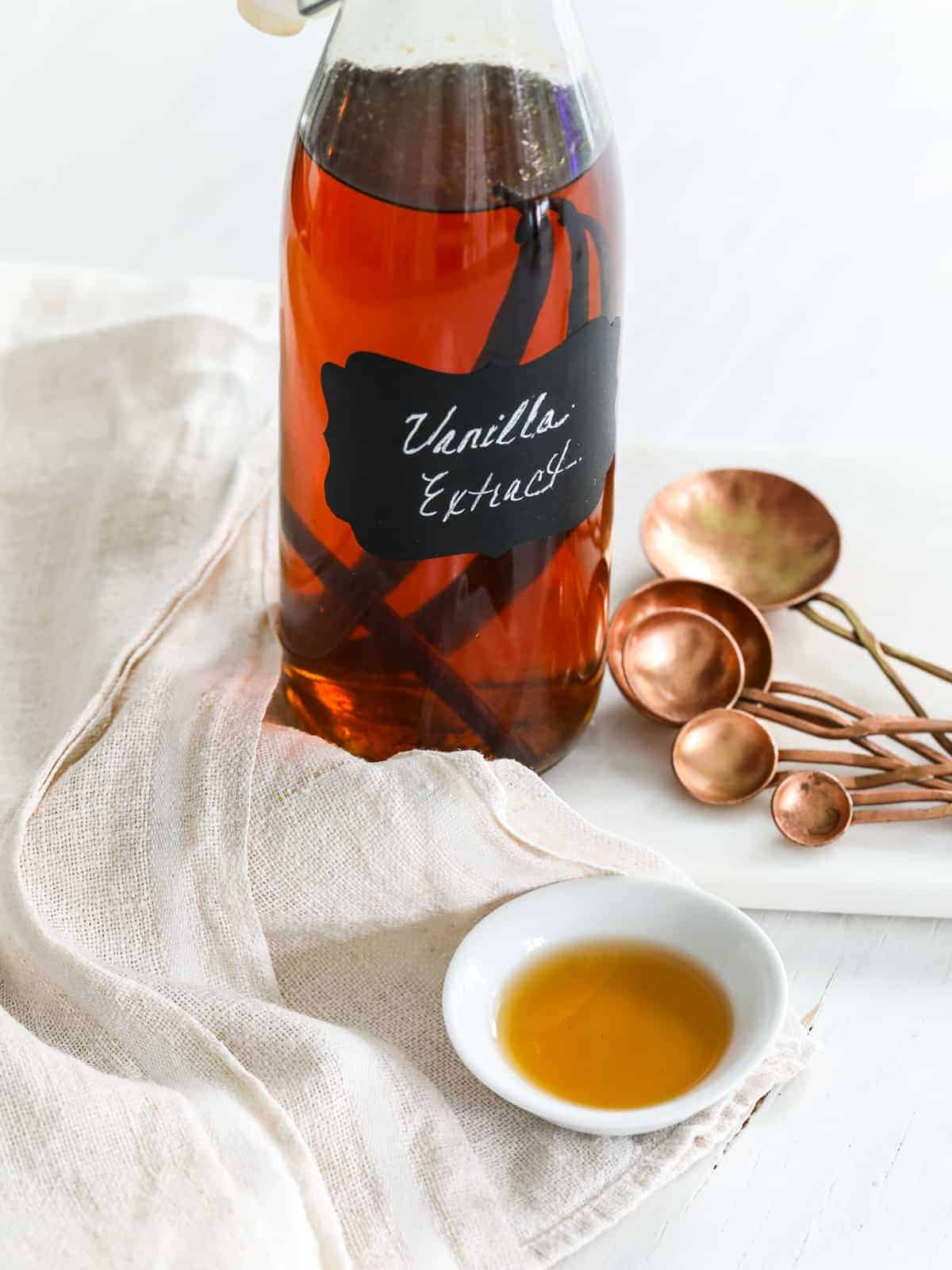 A glass flip top bottle filled with vanilla extract, and real vanilla bean pods on the table.