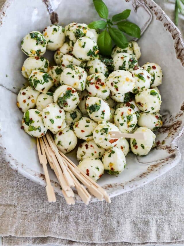 Marinated mozzarella balls in a beige ceramic dish with wooden toothpicks at a party.