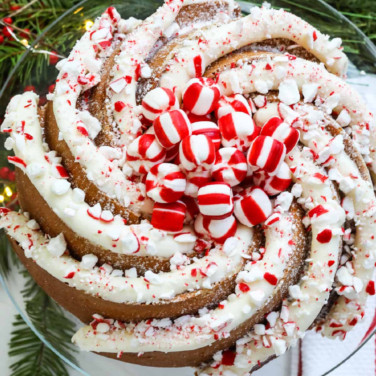 A gorgeous swirl bundt Christmas cake decorated with large piping of peppermint buttercream frosting and crushed and whole candy cane peppermints.