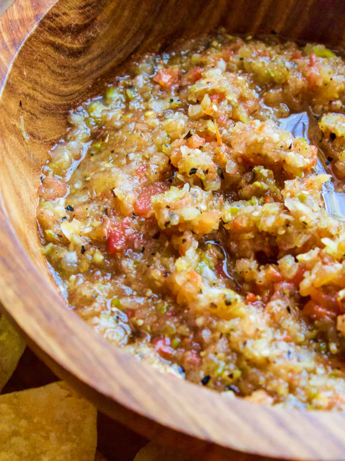 Looking down into a wooden bowl of homemade tomatillo salsa made from 6 ingredients, tomatoes, onions, peppers, garlic, salt, and tomatillos.