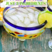 A blue rimmed margarita glass filled with limeade margaritas with a pitcher of margaritas in the background.