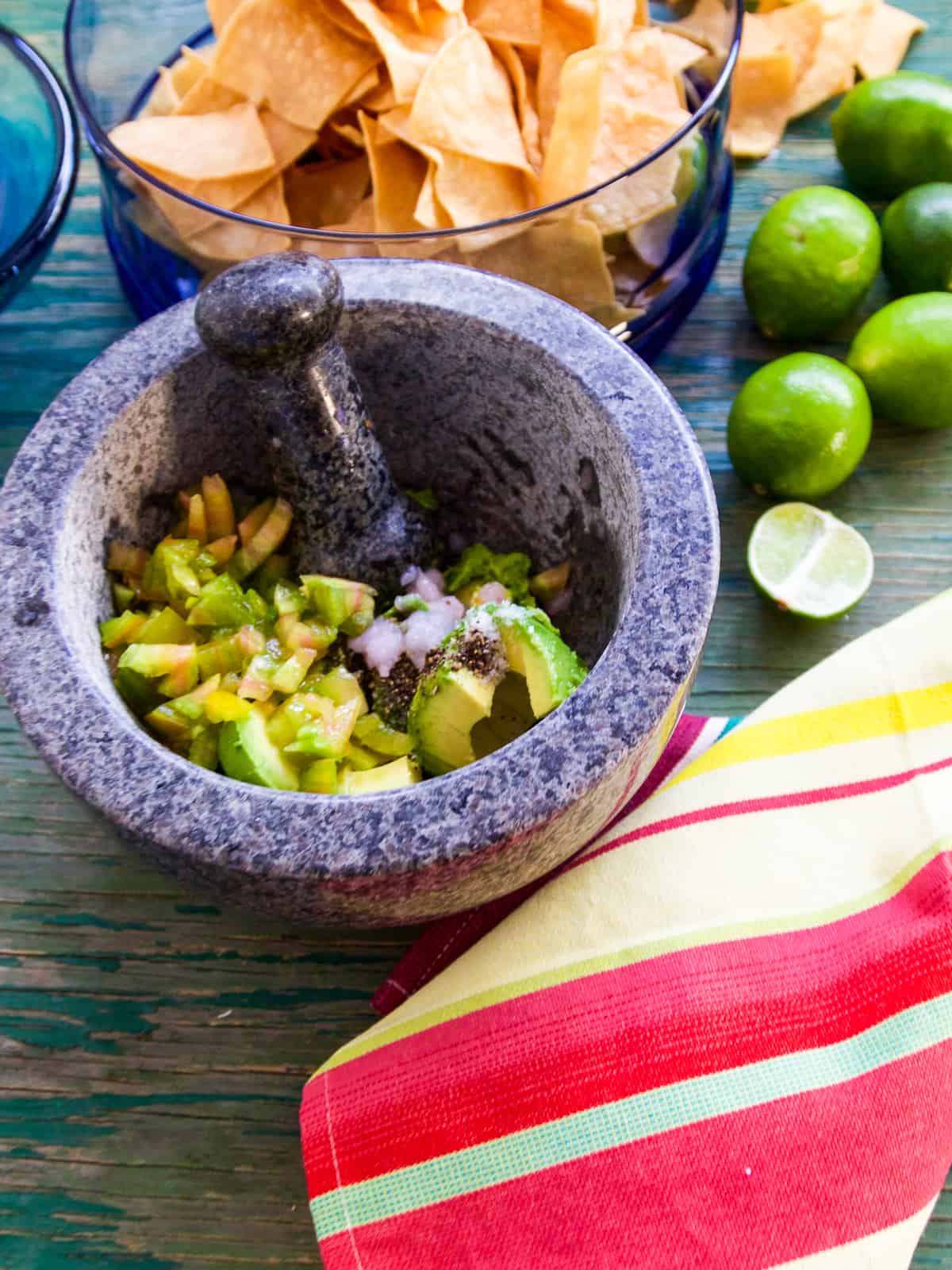 Making guacamole with ripe avocados, limes, spices, and lime juice in a stone mortar and pestle.