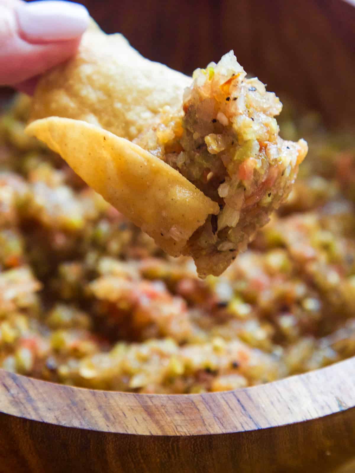 A lady lifting a curved tortilla chip with homemade salsa on it to take a bite.